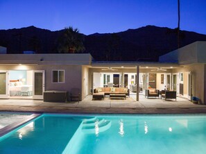 Uma casa moderna com piscina, área de estar no pátio e um quarto com cama e mesa de cabeceira.