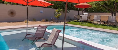 A swimming pool with two lounge chairs and two red umbrellas.