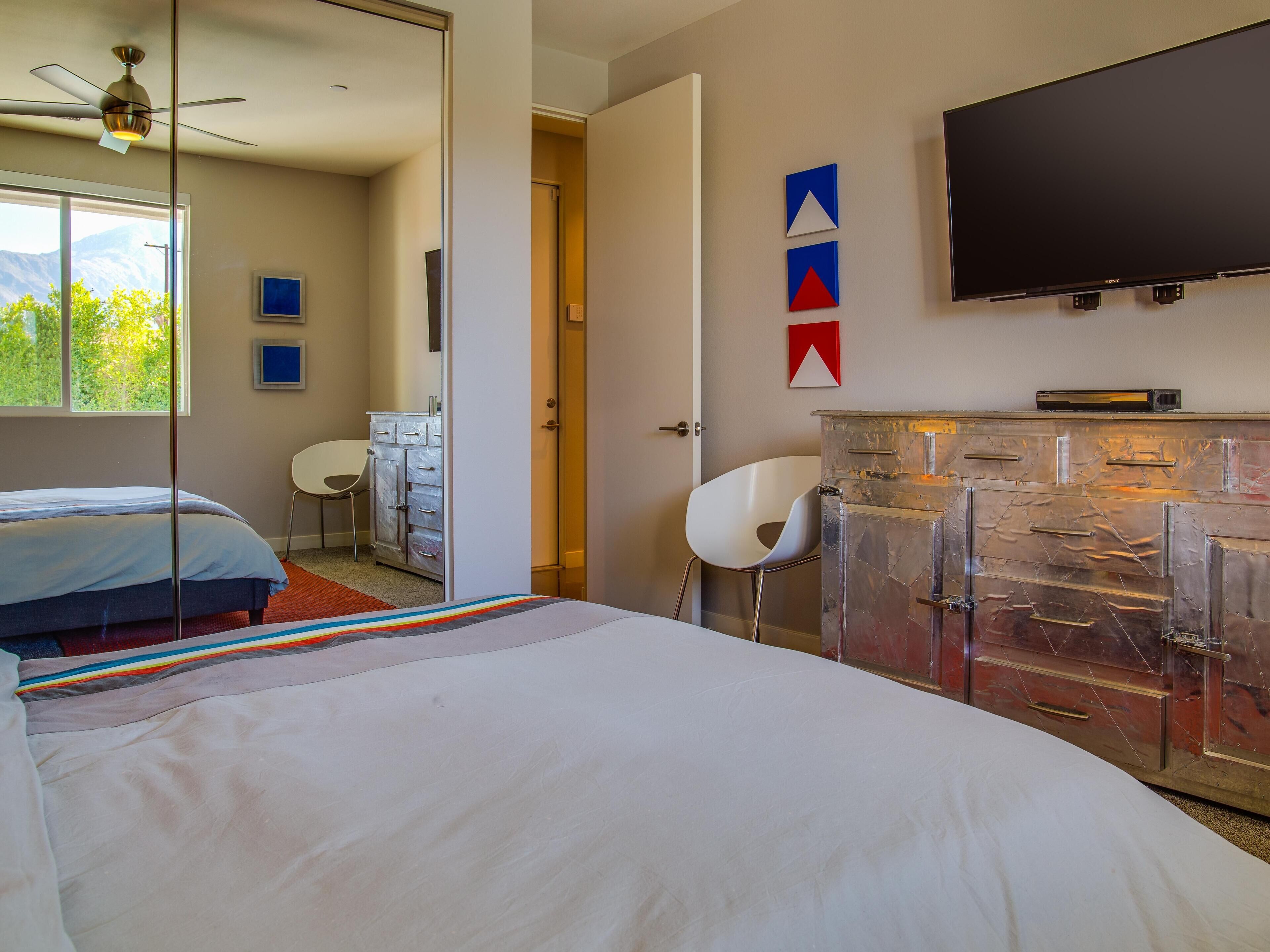 A bedroom with a bed, a desk, a chair, a wardrobe, and a TV.