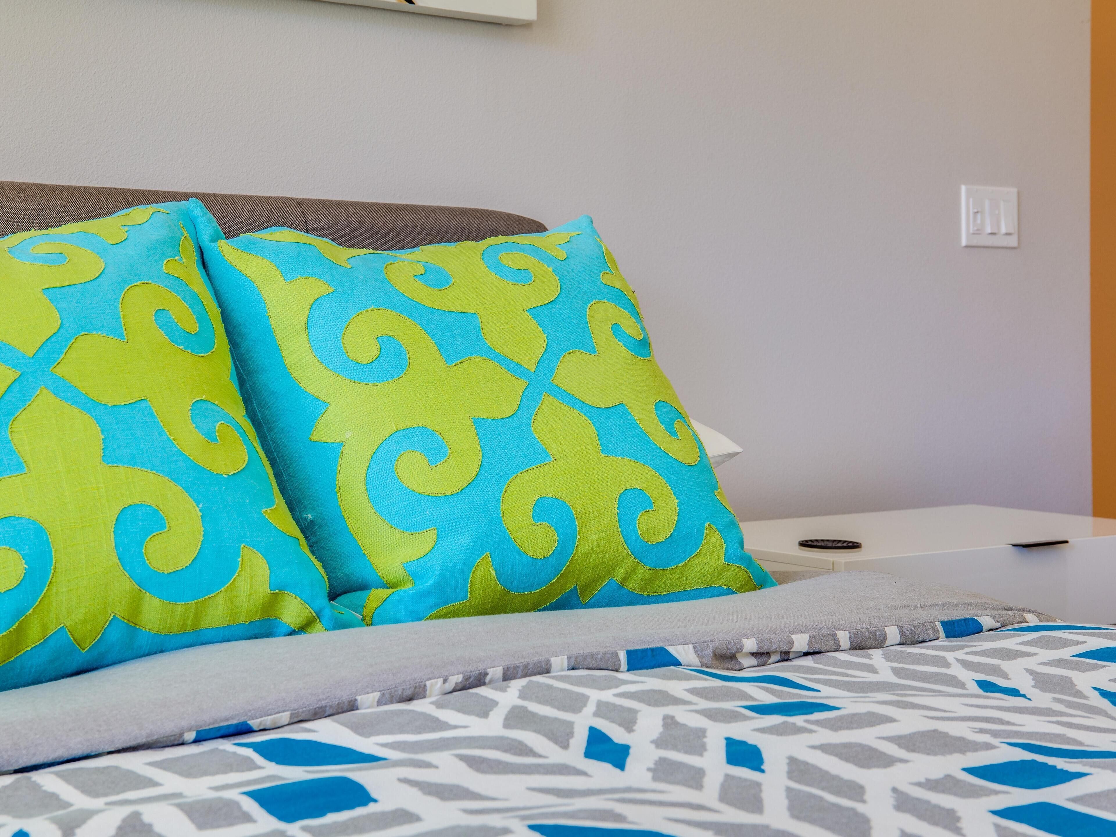 A bed with a patterned bedspread and two pillows with a blue and yellow design.