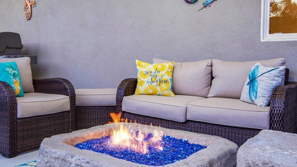 A cozy outdoor seating area with a stone fire pit, wicker furniture, and decorative pillows.