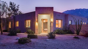 A modern house with a well-lit entrance, surrounded by desert landscaping.