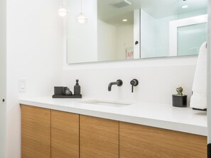 Ein modernes Badezimmer mit einem weißen Waschbecken, Holzschränken, einem Spiegel und Pendelleuchten.