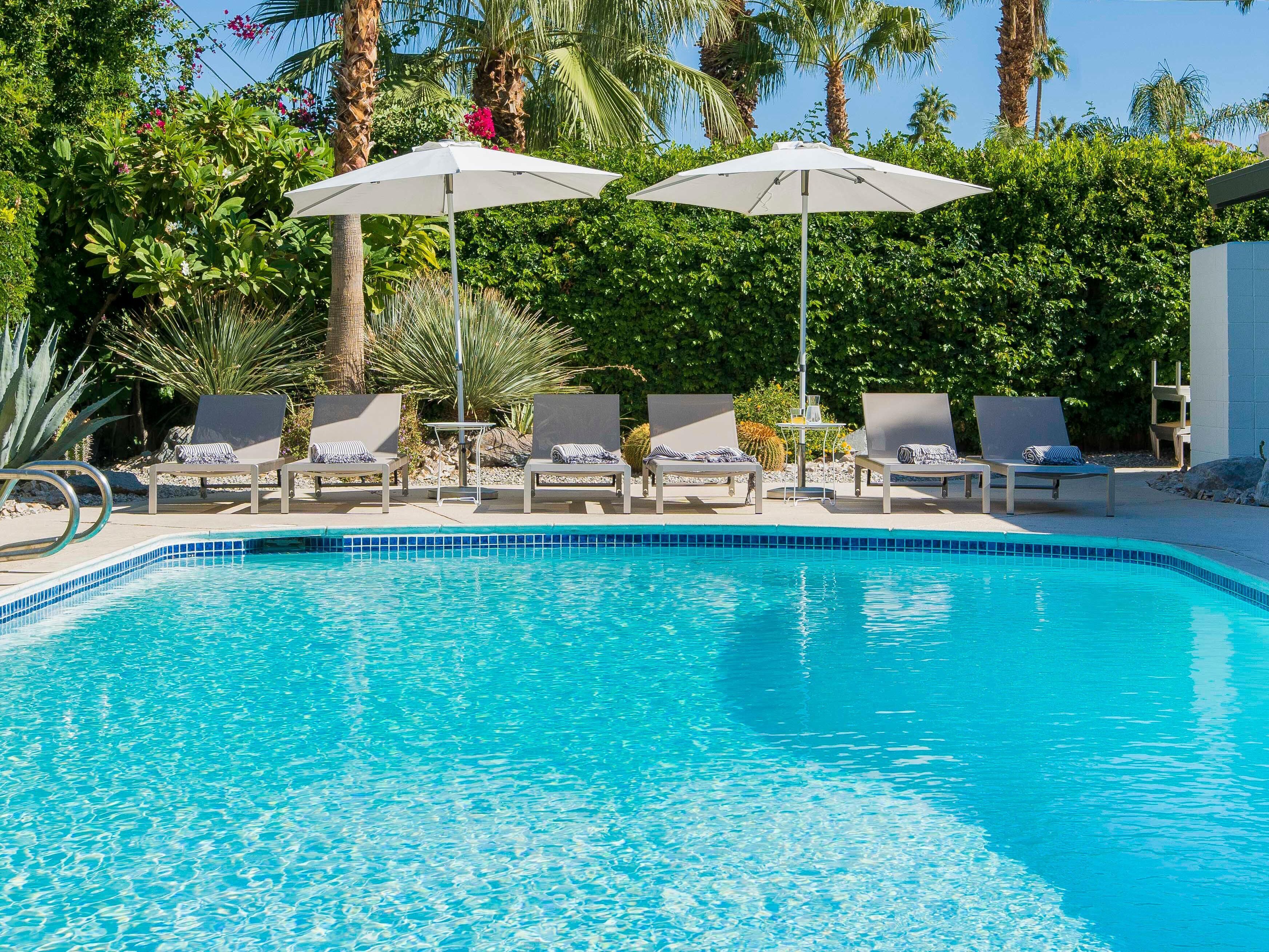A swimming pool with four lounge chairs and two umbrellas.
