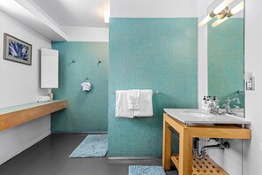 A modern bathroom with a blue tiled wall, a wooden vanity, a white sink, and a mirror. - Lucy I'm Home (Palm Springs)