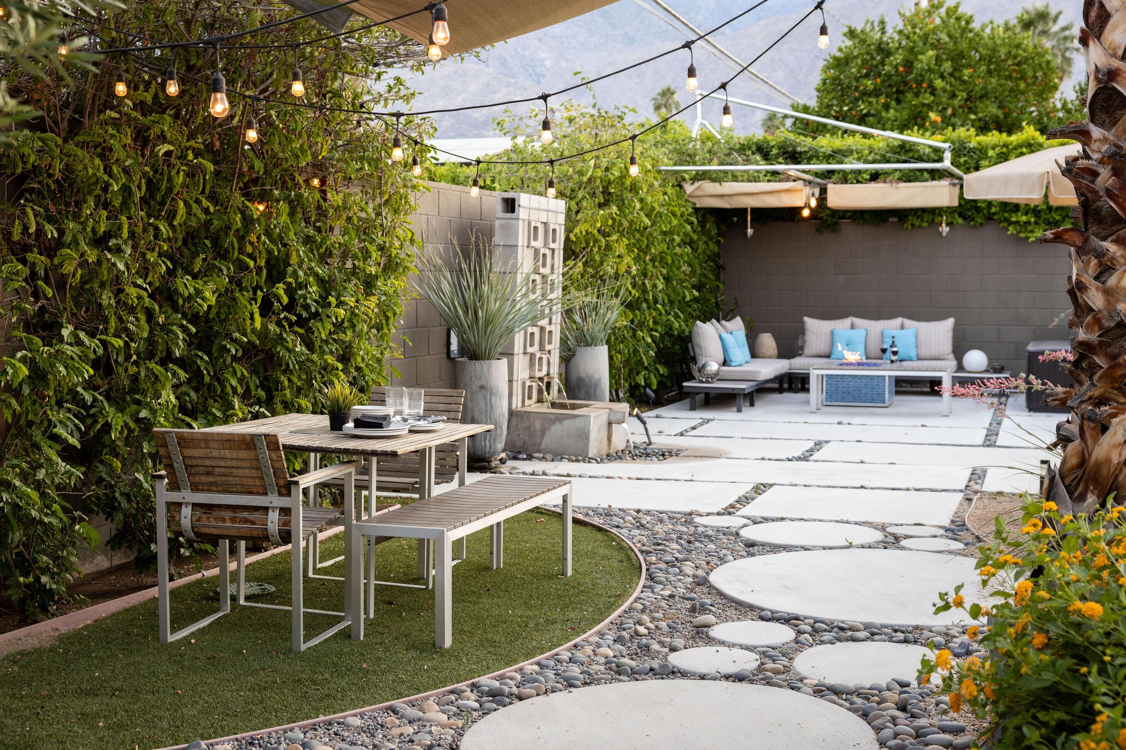 Un patio al aire libre con mesa y sillas de madera, un sendero de piedra y una zona de estar con cojines.