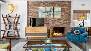 A modern living room with a stone fireplace, a television, and a blue armchair. - Lucy I'm Home (Palm Springs)