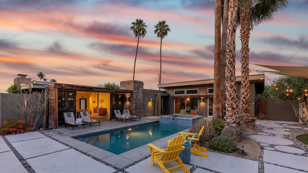 A modern outdoor pool area with a stone deck, lounge chairs, and palm trees. - Lucy I'm Home (Palm Springs)