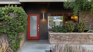 A modern house entrance with a red door, a stone wall, and a well-maintained garden. - Lucy I'm Home (Palm Springs)