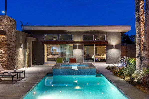 A modern house with a swimming pool, outdoor seating, and a well-lit patio area. - Lucy I'm Home (Palm Springs)