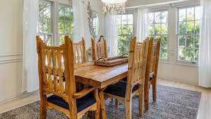Uma sala de jantar com mesa e cadeiras de madeira, janelas amplas e um candelabro.