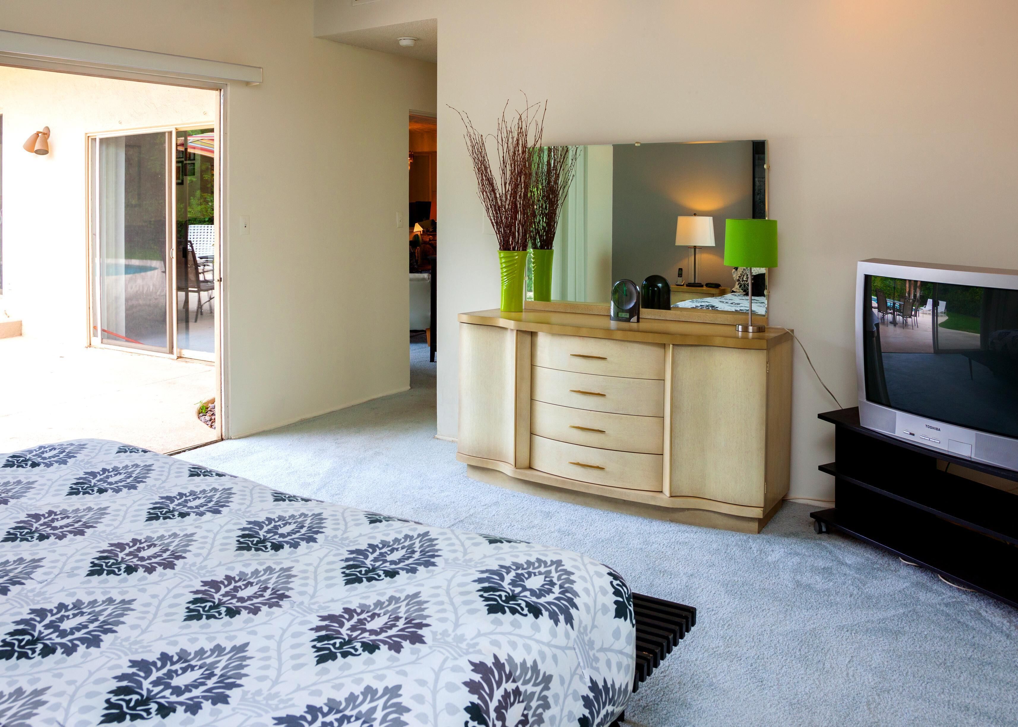 Une chambre à coucher comprenant un lit, une commode, un téléviseur et une porte-fenêtre coulissante donnant sur un patio.