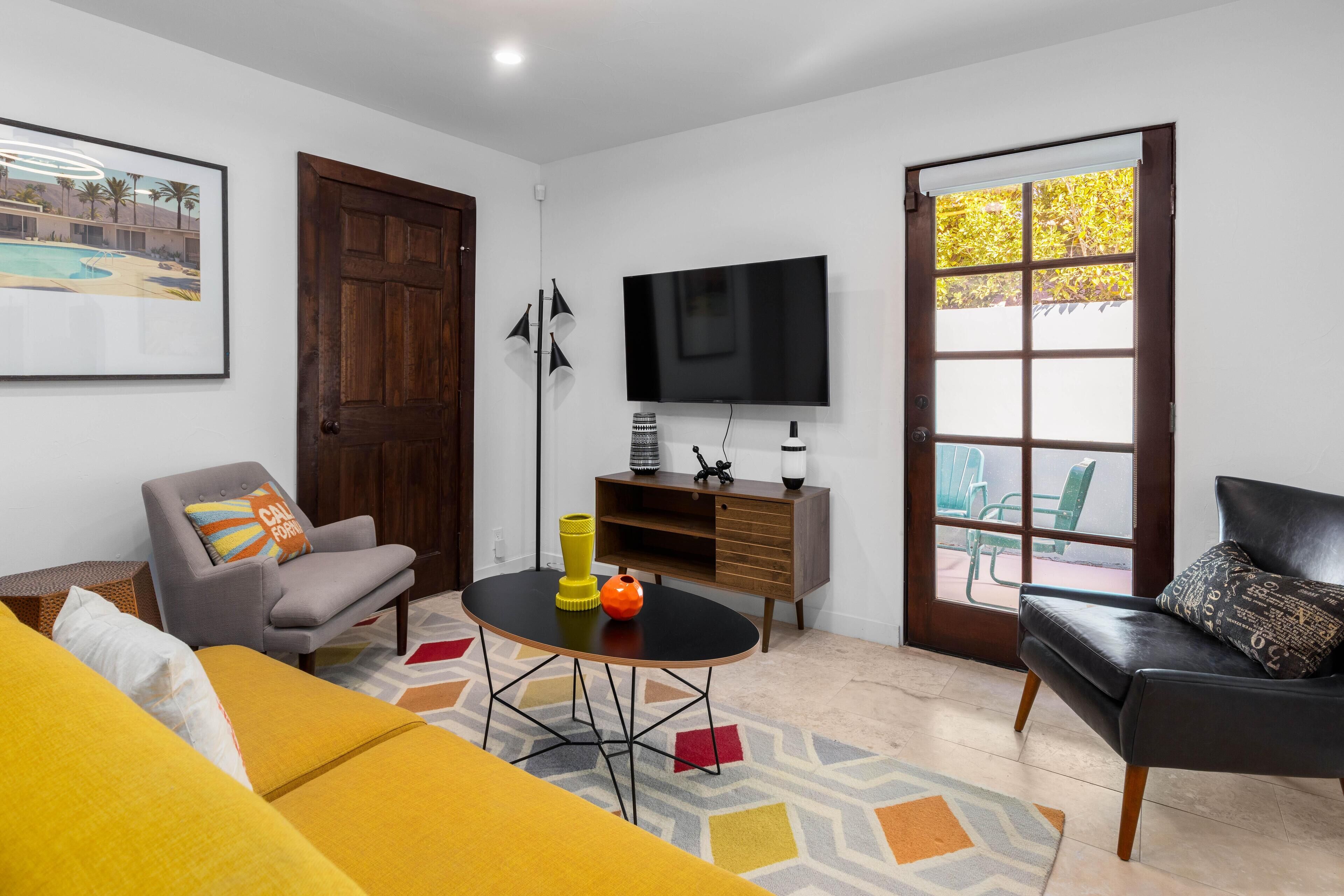 A living room with a sofa, a coffee table, a TV, and a door leading to an outdoor area.