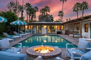 A pool area with lounge chairs, a fire pit, and a building with large windows. - The Clever Cactus (Palm Springs)