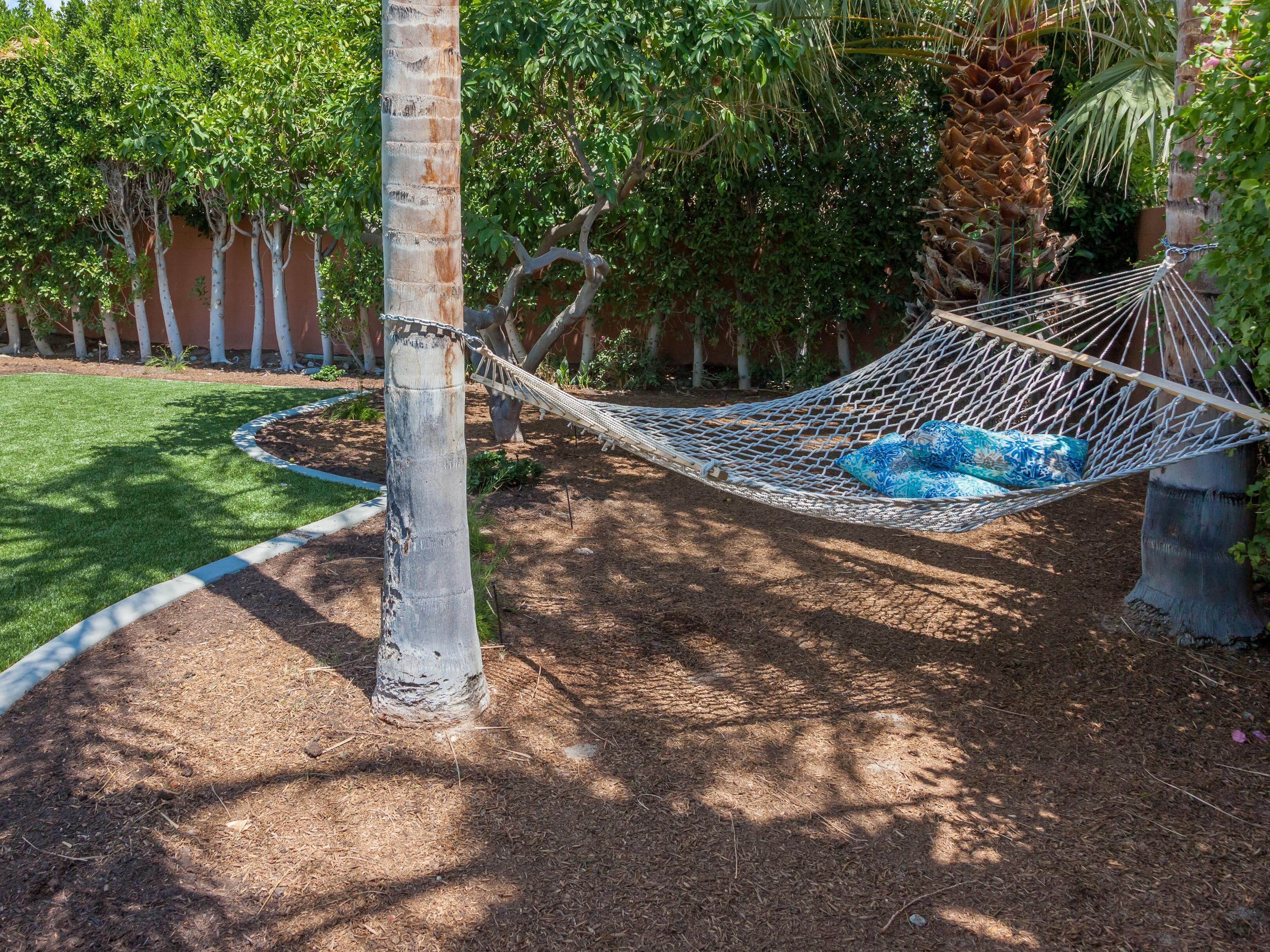 A hammock tied between two trees in a landscaped garden with a well-maintained lawn and a variety of plants.