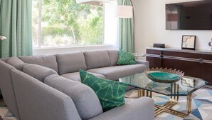 A modern living room with a grey sectional sofa, a glass coffee table with a green decorative bowl, and a TV mounted on the wall.