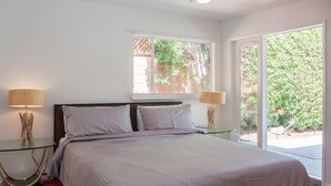 A bedroom with a bed, two bedside tables, and a window with a view of greenery.