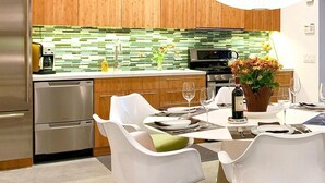 A modern kitchen with wooden cabinets, a stainless steel refrigerator, and a green-tiled backsplash. - Glass and Steel House 2012 (Palm Springs)