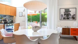 A modern kitchen with a round dining table, white chairs, and a pendant light. - Glass and Steel House 2012 (Palm Springs)