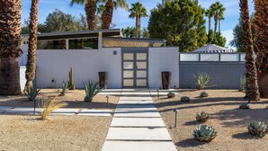 A modern building with a white exterior, a large glass door, and a pathway leading to the entrance. - Happy Hour (Palm Springs)
