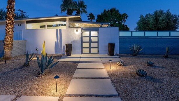 A modern house with a concrete pathway leading to the entrance, surrounded by desert plants and palm trees. - Happy Hour (Palm Springs)