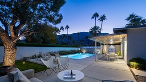 A modern outdoor living area with a pool, seating, and a covered patio. - Happy Hour (Palm Springs)
