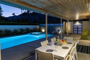 Un espace extérieur avec une piscine, une table dressée pour les repas, entourée de chaises, et une terrasse couverte.