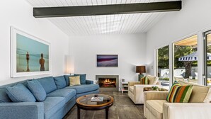 A modern living room with a blue sofa, a beige armchair, a round coffee table, and a fireplace. - Happy Hour (Palm Springs)