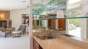 A modern kitchen with a glass backsplash, stainless steel sink, and a dining area with patterned chairs.