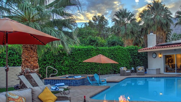 A pool area with lounge chairs, a fire pit, and a hot tub.