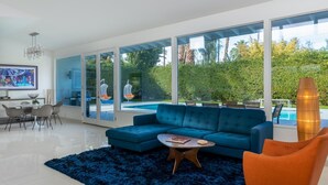 Un salon moderne avec un canapé bleu, une table basse et une grande fenêtre donnant sur une piscine et un espace verdoyant.