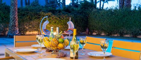 Une table à manger d’extérieur, dressée avec des assiettes, des verres et un saladier rempli de fruits.