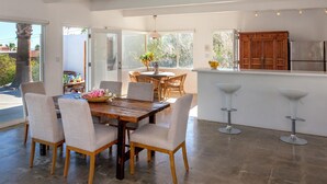 A modern kitchen with a wooden island, bar stools, and a dining area with a wooden table and chairs. - Hilltop Haven (Palm Springs)