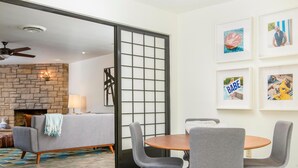 A modern living room with a fireplace, a dining area with a round table and chairs, and a large sliding glass door leading to an outdoor space. - Canary Palms (Palm Springs)