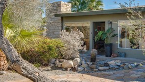 A modern house with a stone facade, a stone patio, and a variety of plants and cacti in the garden. - Canary Palms (Palm Springs)