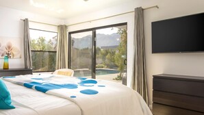A bedroom with a bed, a TV, a balcony with a pool, and a mountain view. - Casa Azul (Palm Springs)