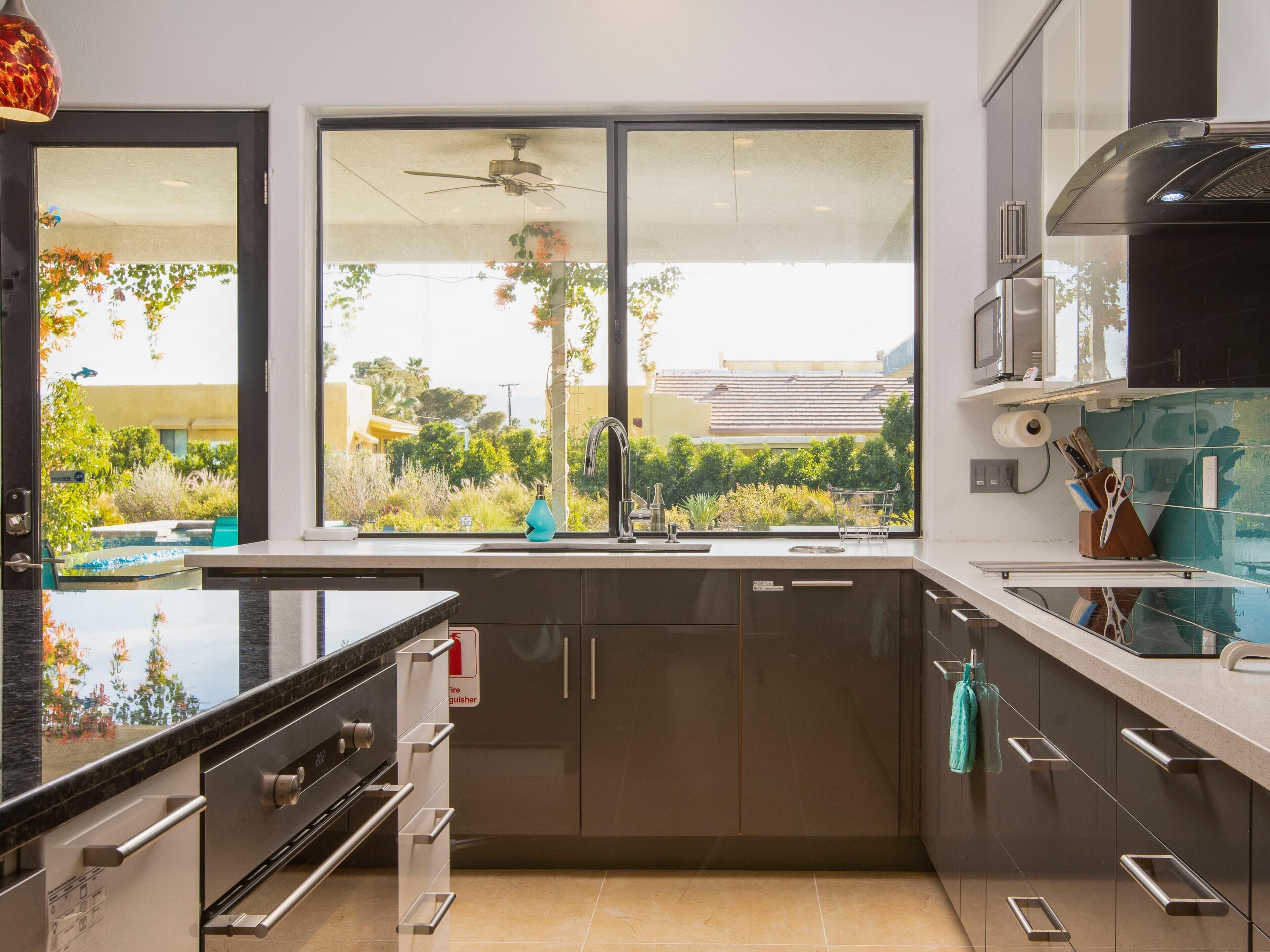 A modern kitchen with a large window, stainless steel appliances, and a view of a landscaped garden.