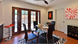 A dining area with a glass table, four chairs, a ceiling fan, and a red bar stool. - Zen Dreams (Palm Springs)