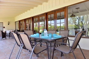 A covered patio with a table set for four, surrounded by cushioned chairs, large windows, and a stone floor. - Zen Dreams (Palm Springs)