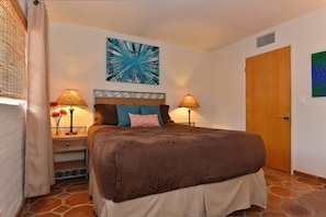 A bedroom with a large bed, two bedside lamps, a wooden headboard, a wall art piece, and a door. - Zen Dreams (Palm Springs)