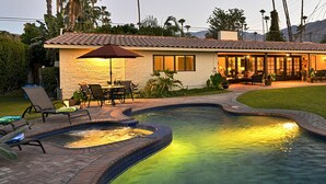 A swimming pool with a curved design, surrounded by a brick patio and lounge chairs. - Zen Dreams (Palm Springs)