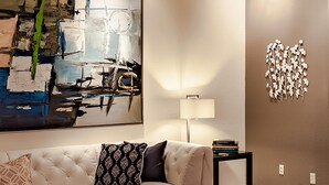 A modern living room with a beige sofa, a glass coffee table, and a large abstract painting on the wall. - Andiamo al Sole (Palm Springs)
