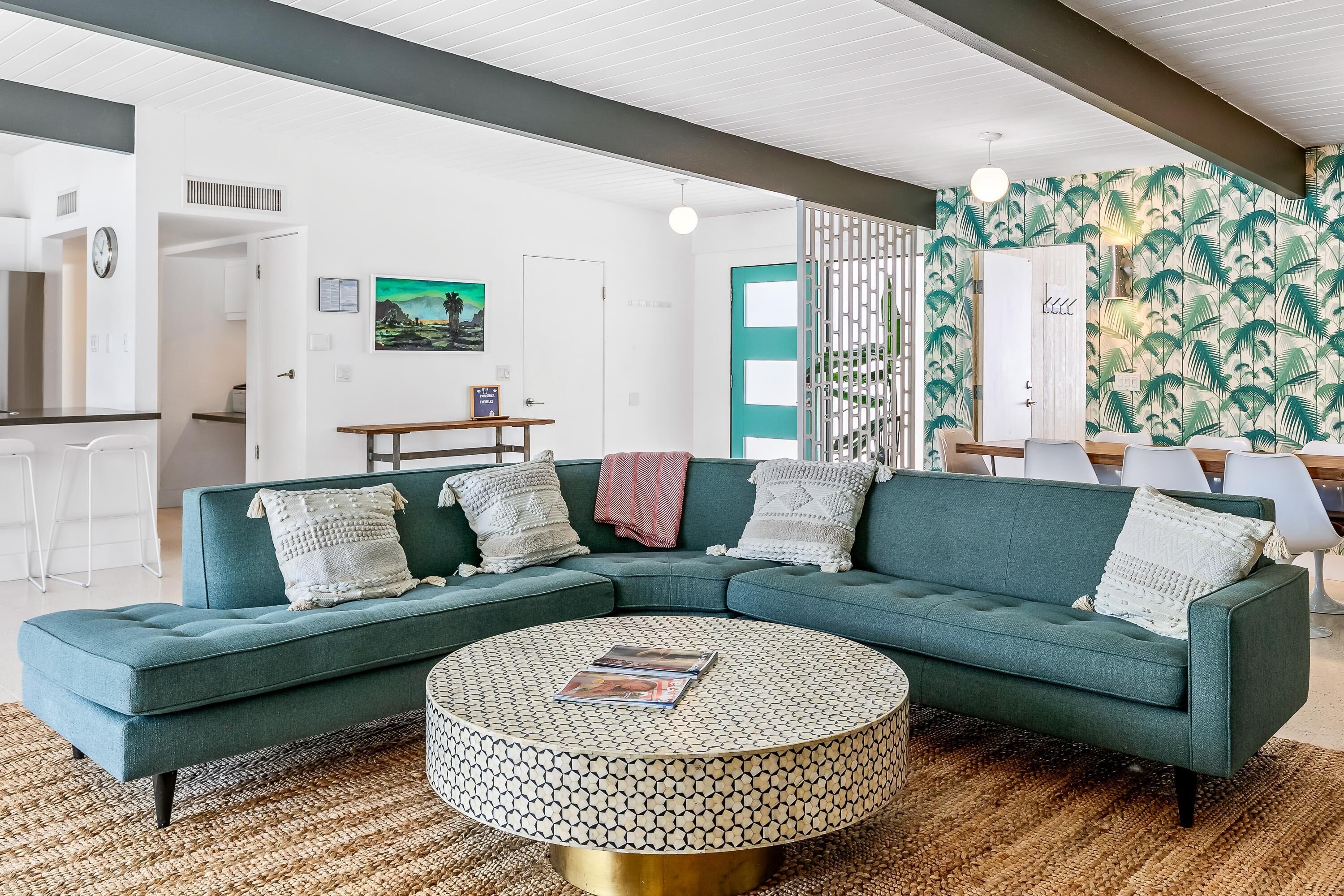 Een moderne woonkamer met een smaragdgroene modulaire bank, een bijzettafeltje met een patroon en een tropische behangwand.