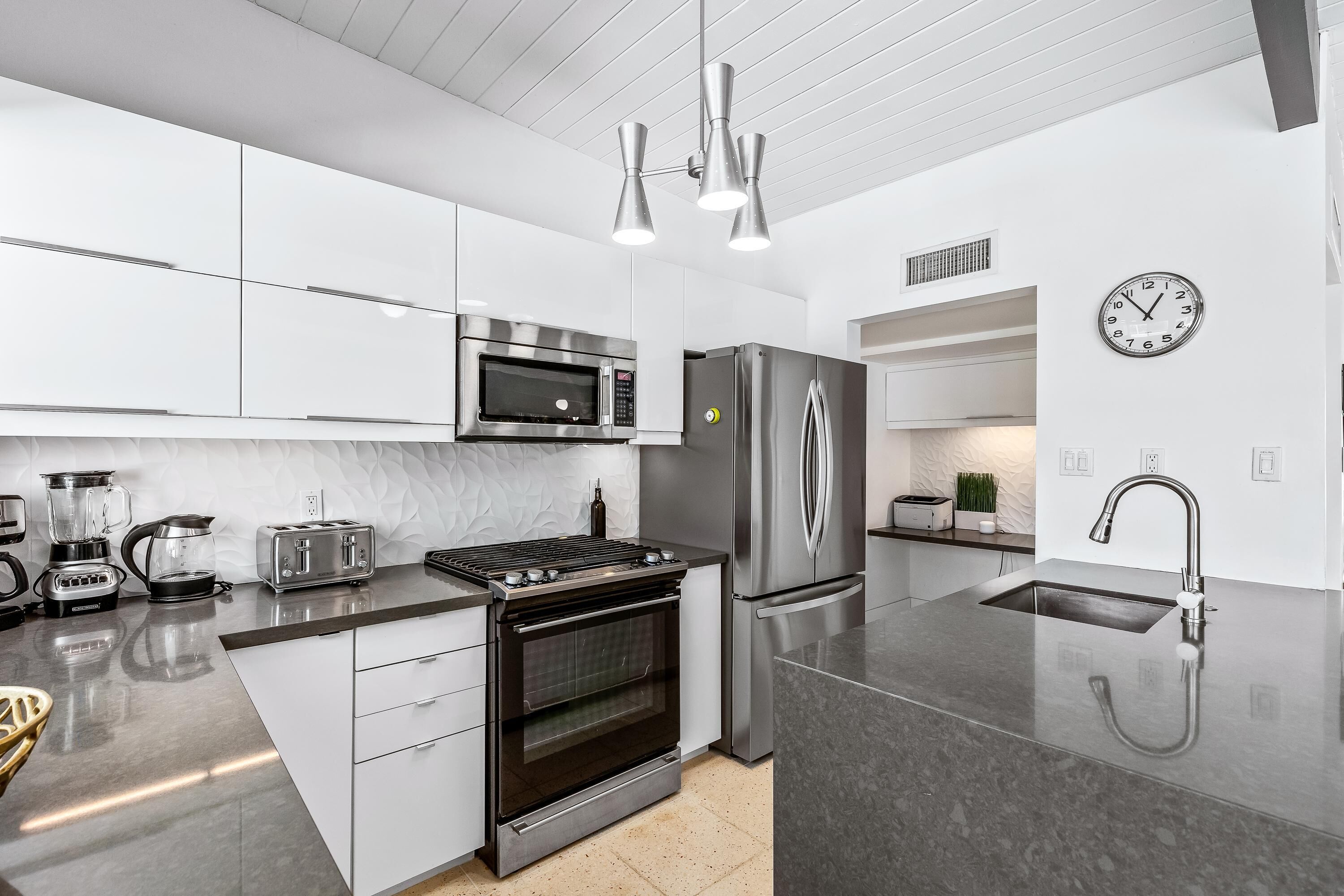 Una cocina moderna con electrodomésticos de acero inoxidable, horno empotrado, una isla grande con fregadero e iluminación colgante.