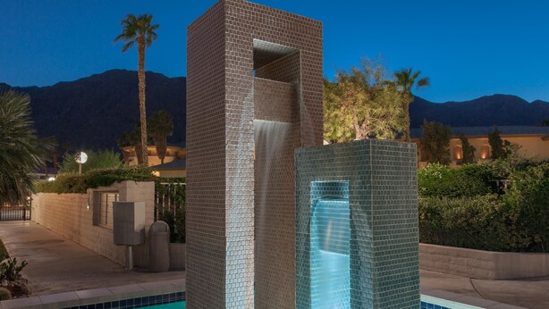 A modern pool area with a central water feature and a brick structure.