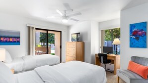 A hotel room with two beds, a desk, a chair, a ceiling fan, and a large window.