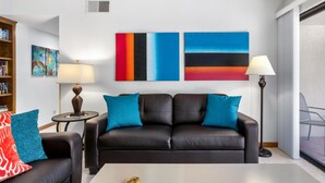 A modern living room with a black leather sofa, two blue cushions, a coffee table, and a bookshelf.