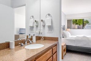 A hotel bathroom with a granite countertop sink, a large mirror, and a hairdryer.