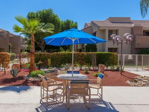 An outdoor patio with a round table and four chairs, a blue umbrella, and a palm tree.