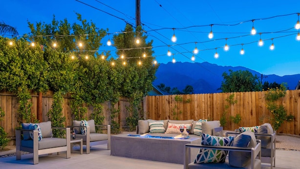 Patio esterno con recinzione in legno, luci a stringa e mobili da giardino.